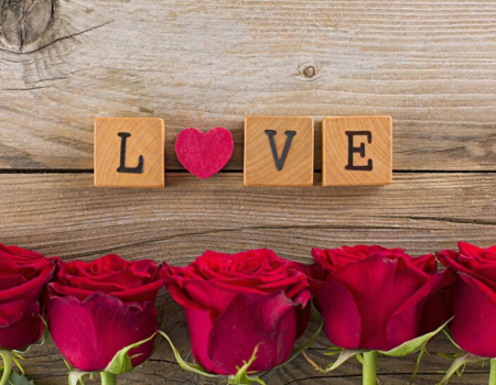 wood blocks spelling out "love" surrounded by red roses